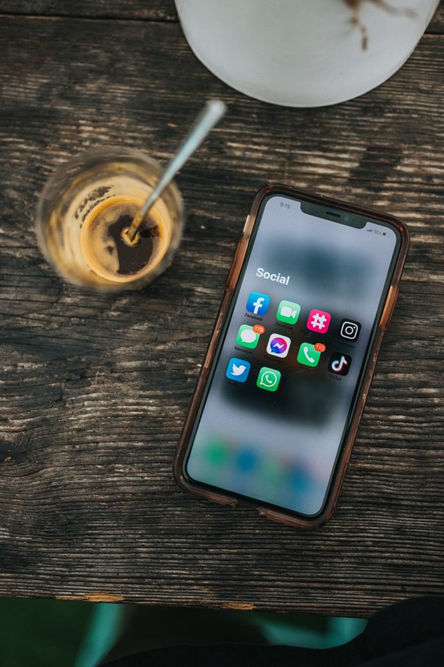 A phone on a table with social media icons shown on a screen and the phone is next to a coffee